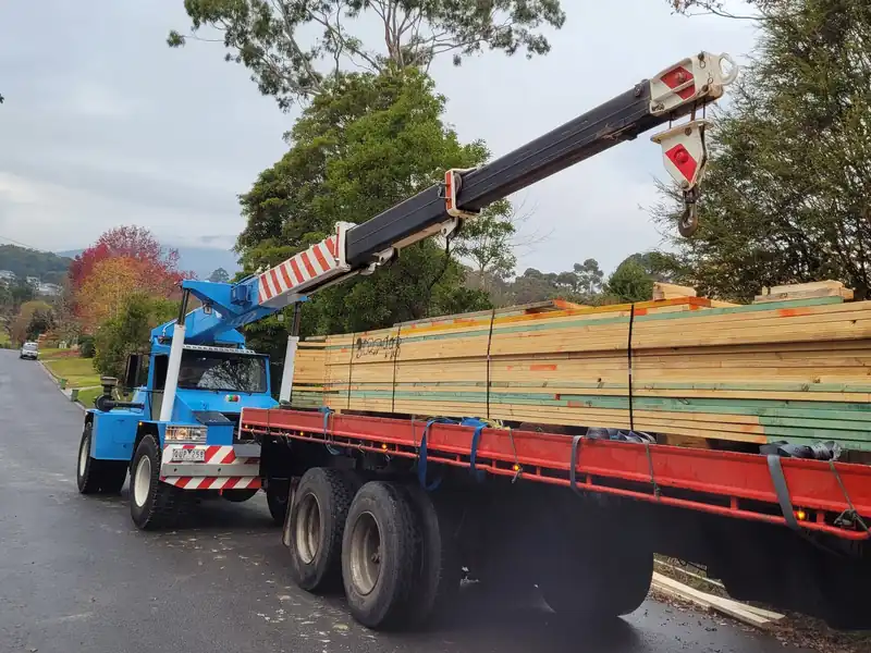 Blue Franna crane beside a trailer stacked with timber packs