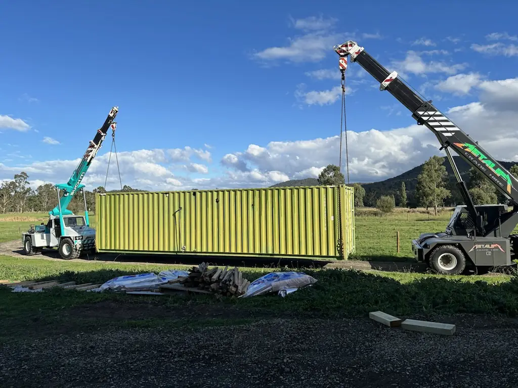 Two Ranges Rigging cranes lifting a lime-green shipping container in a paddock
