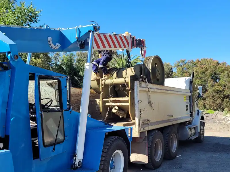 Blue crane lifting a piece of plant equipment off the back of a tipper truck