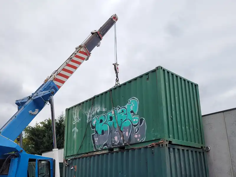 Blue crane stacking a green shipping container on top of another