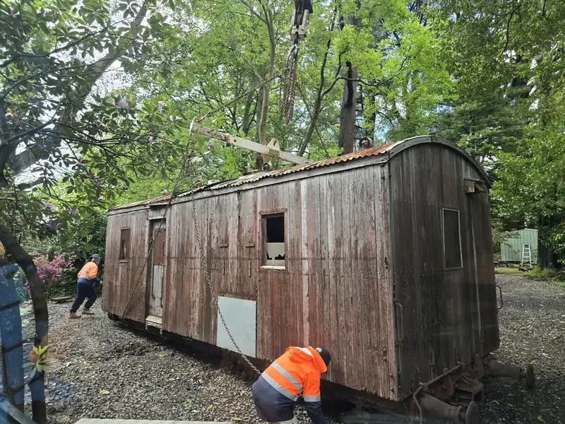 Two workers in hi-vis rigging an old timber hut for a lift